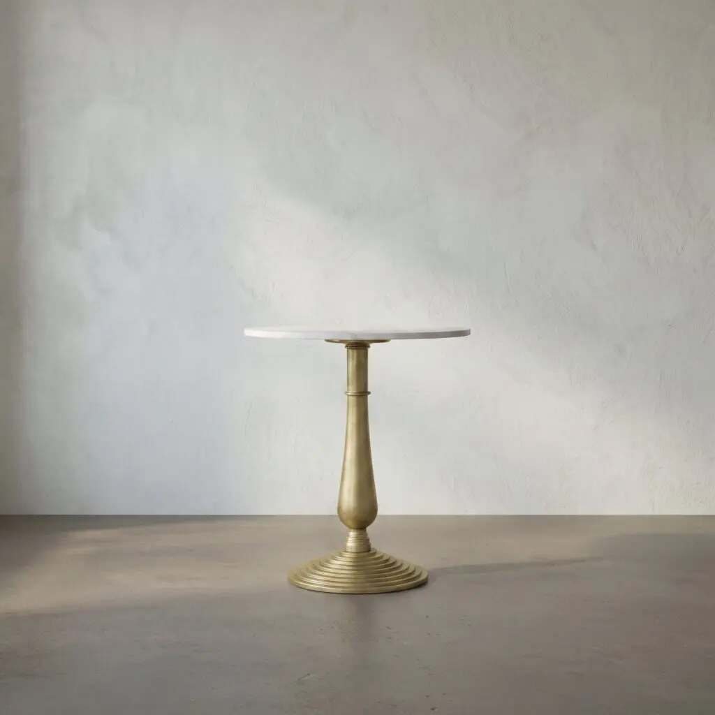 Gold pedestal table with a round white top centered against a textured gray wall, empty surface above a concrete floor.