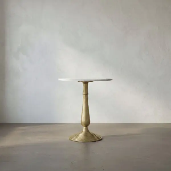 Gold pedestal table with a round white top centered against a textured gray wall, empty surface above a concrete floor.