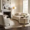 Neutral living room with beige sofas, cream armchairs, a marble fireplace, and a large abstract painting above the mantel.