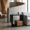 Modern living area with a curved wooden console against a concrete wall, books and a small vase on a black table in the foreground.