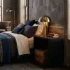 Luxurious hotel bedroom with dark wood walls, brass bedside lamp, and a stack of books on a nightstand beside the bed.
