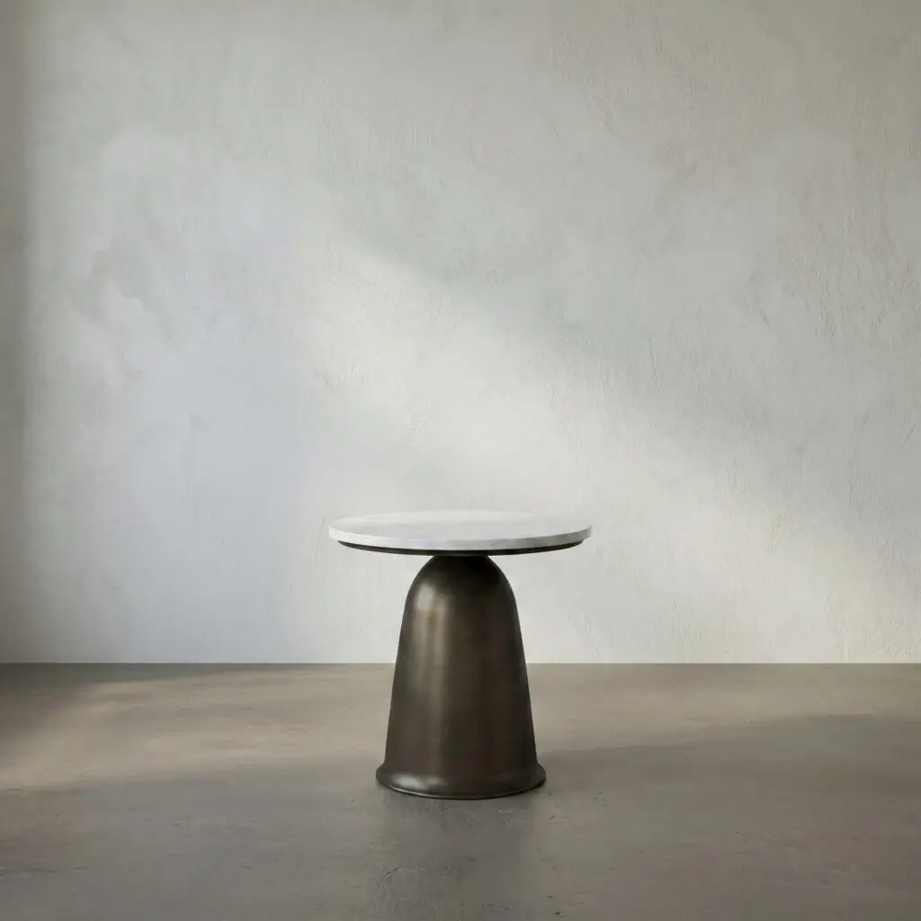 Round marble-topped pedestal table with a dark, curved base against a gray textured wall and concrete floor.