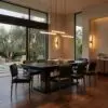Modern dining room with a long black table, black chairs, and warm pendant lights, large windows showing greenery outside.