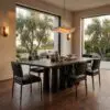 Sunlit dining room with a dark wood table and black chairs, large windows showing trees outside, and ceramic vases on the table.