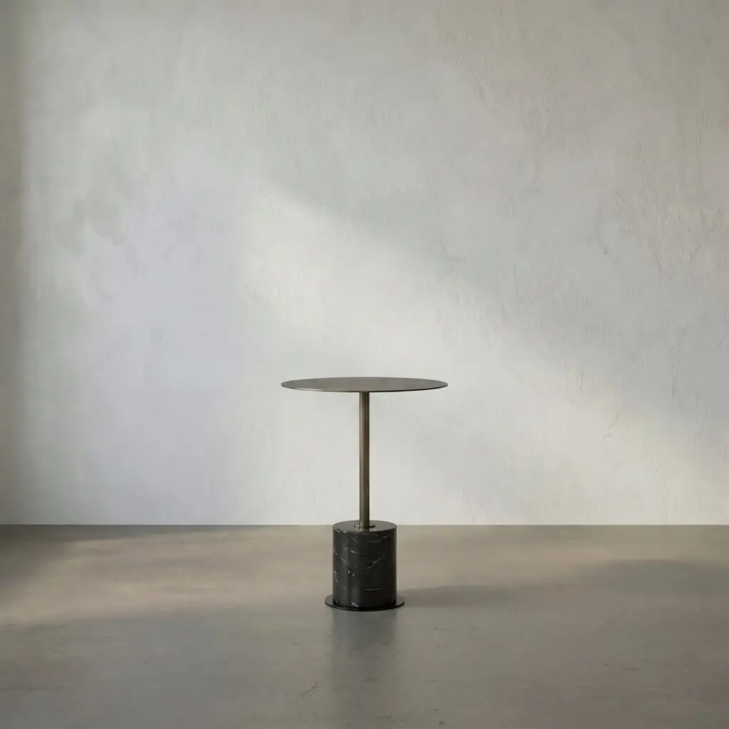 Round tabletop on a slender pedestal with a black marble base in a sparse gray room.