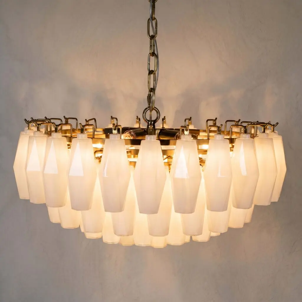 A close-up of a hanging chandelier with many white geometric lamps and metal chains against a neutral wall.