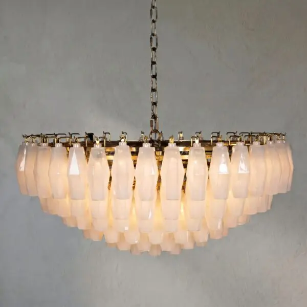 Chandelier with many frosted glass shades hanging from a metal chain against a gray wall.