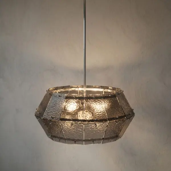 Metallic geometric pendant lamp with hammered panels hanging from the ceiling, against a textured wall.