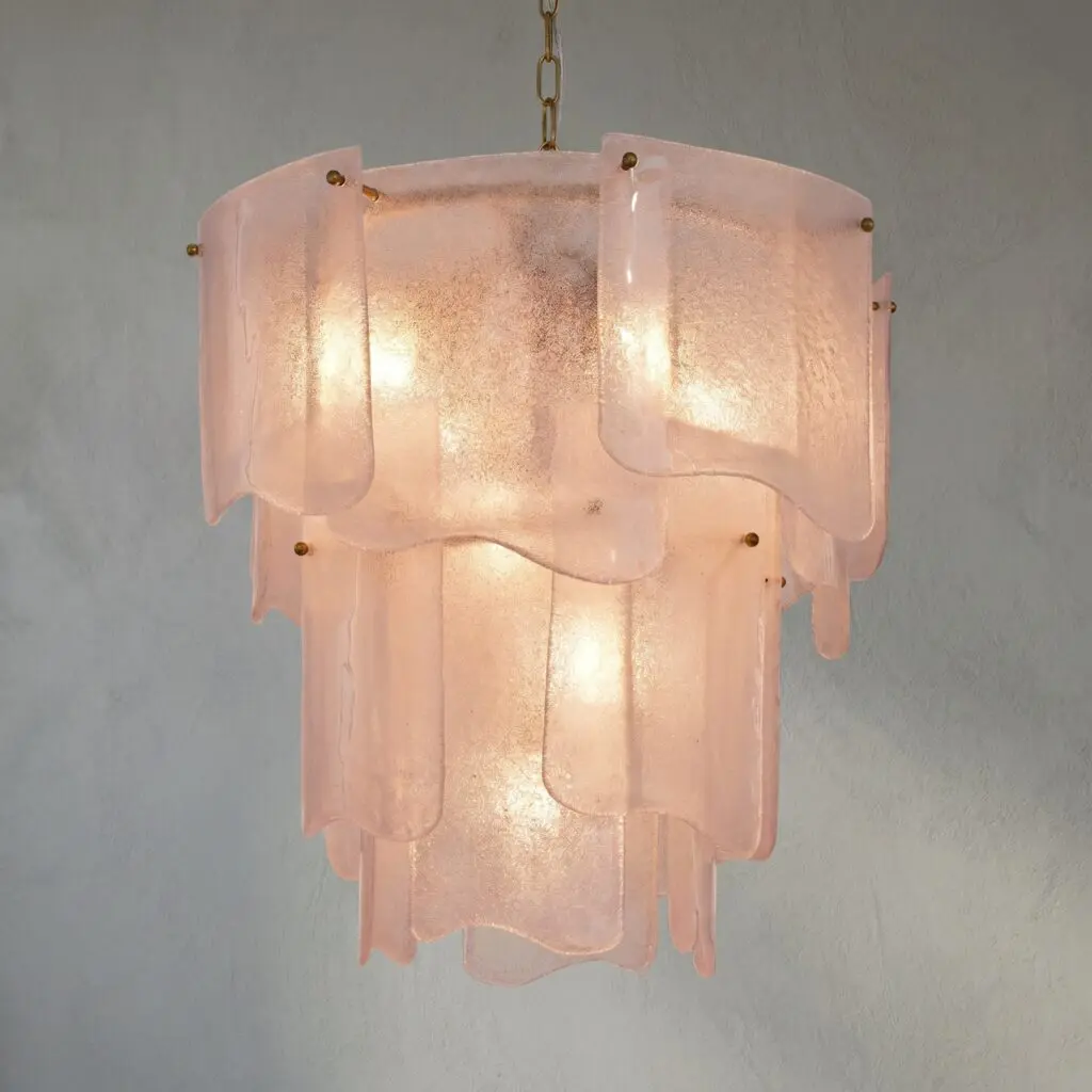 Pink frosted glass pendant lampshade suspended by a brass chain against a gray wall.