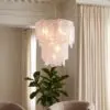 Soft frosted glass pendant chandelier hanging from a chain in a living room with beige curtains and a leafy indoor plant nearby.