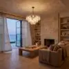 Living room with a glass chandelier lit, hanging above a wooden coffee table, warm tones throughout a stone fireplace and shelves.
