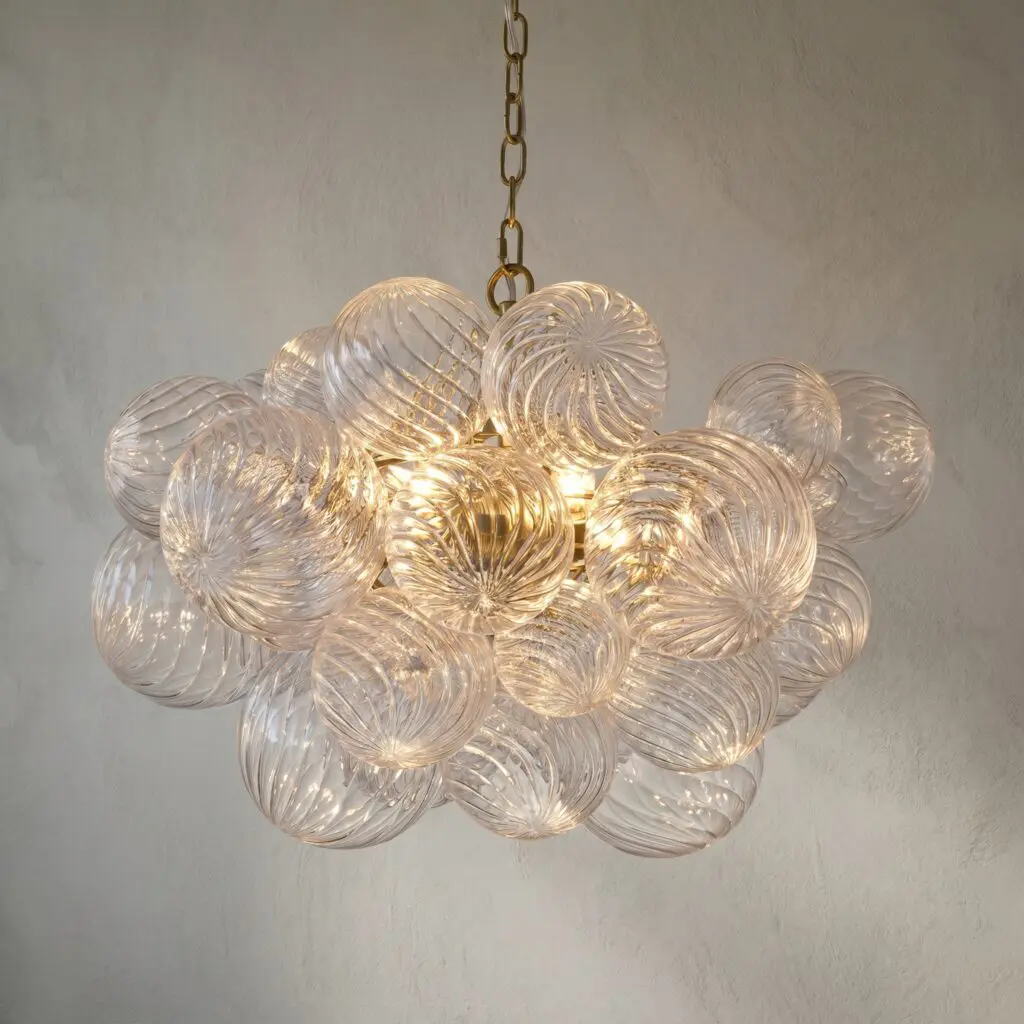 Close-up of a hanging chandelier with clear ribbed glass spheres and brass chain against a textured wall
