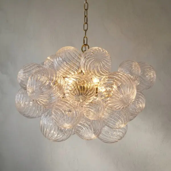 Close-up of a hanging chandelier with clear ribbed glass spheres and brass chain against a textured wall