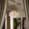 Elegant interior with a chain-hung glass globe chandelier, cream curtains, and panelled walls; a potted plant sits nearby.