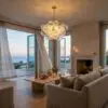 Cozy living room with beige sofas, a wooden coffee table, and a glass bubble chandelier, opening to an ocean view.