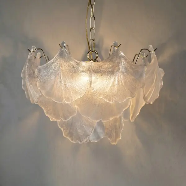 Chandelier with frosted, scalloped glass shades hanging from brass chains, lit warmly against a gray wall as seen from below.