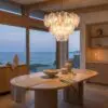 Wood dining table with a linen runner and ceramic bowls, set beside large windows looking out to the sea; a glass railing outside.