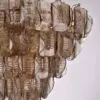Close-up of a glass chandelier with overlapping ribbed leaf-shaped shades and a gold chain structure.