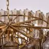 Close-up of a gold metal chandelier frame with glass prisms hanging from chains and riveted arms.
