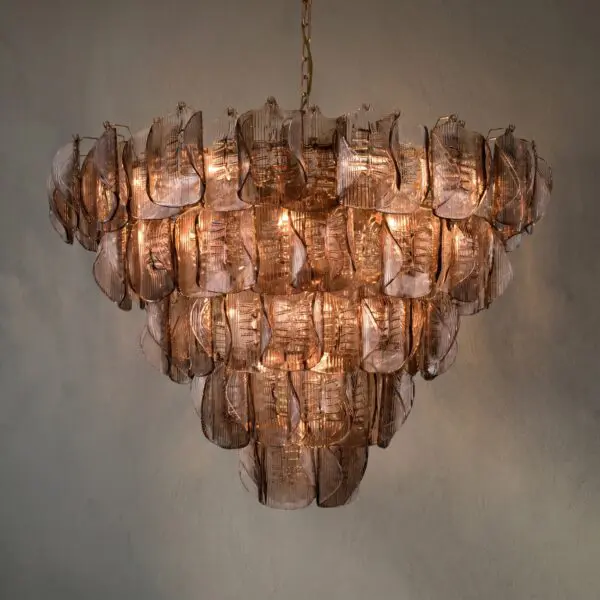 Copper-toned glass chandelier with layered petal-like prisms hanging from a chain, lit warmly against a neutral wall.