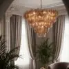 Luxurious chandelier with layered glass petals hanging in a classic room, surrounded by curtains and greenery in soft light.