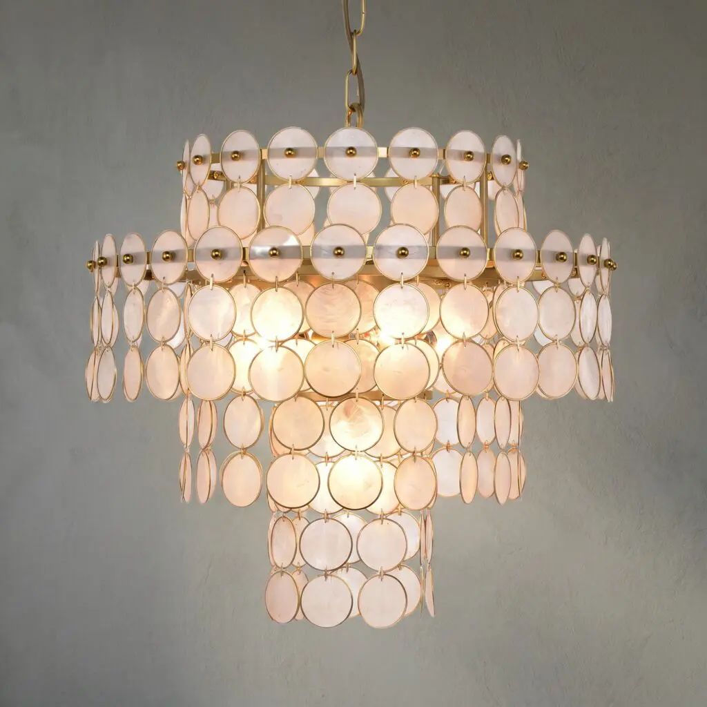 Gold chandelier with multiple circular white discs arranged in tiers, hanging from a chain against a gray wall.