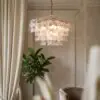 Elegant chandelier with frosted square panels hanging from a chain in a softly lit living room corner, next to cream curtains and a green plant.