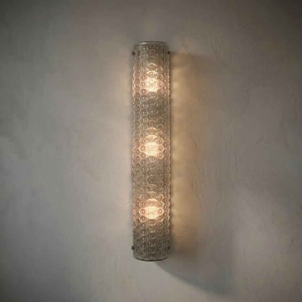Tall cylindrical lamp with circular bubble pattern, casting warm light on a textured wall behind it.