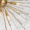 Close-up of a gold chandelier with glass bulbs and radiating rods across a light background.