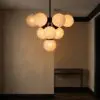 Modern globe chandelier with warm amber lights hanging above a dark staircase in a dim hallway, contemporary interior lighting.