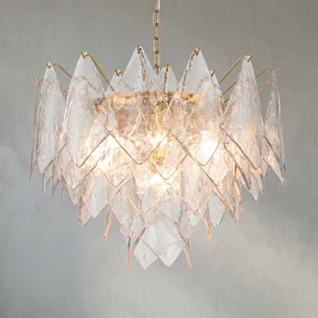 Crystal chandelier with clear glass prisms and gold metal accents hanging from a chain against a gray wall.