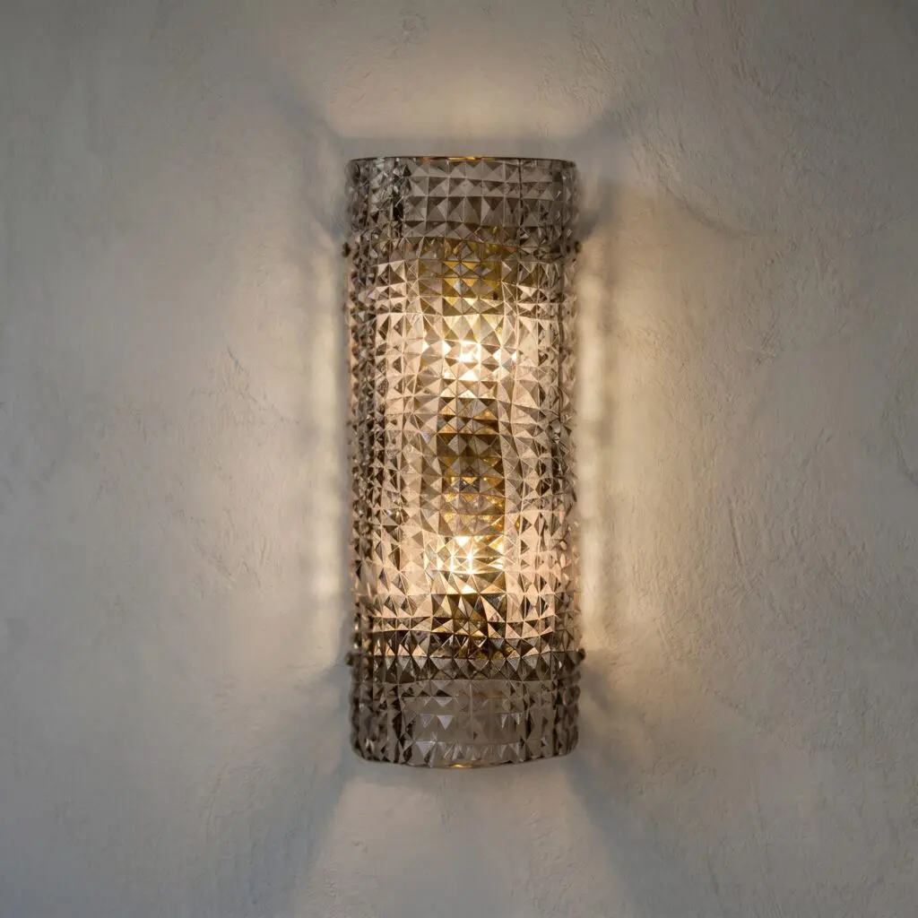 Metal wall sconce with a triangular geometric pattern, emitting warm light on a textured wall.