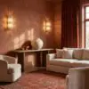 Corner of a warm living room with terracotta walls, crystal wall lamps, a wooden console holding a large beige vase and small bowls, and a red rug with beige seating nearby.