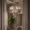 Metallic disc chandelier hanging from a chain in a beige-paneled living room with curtains on both sides.