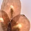 Close-up of copper-toned metallic leaves with pronounced veins, softly lit from beneath, decorative arrangement.