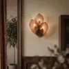 Copper leaf-shaped lamp casting warm light on a beige textured wall, framed by dark wood panels and furniture.