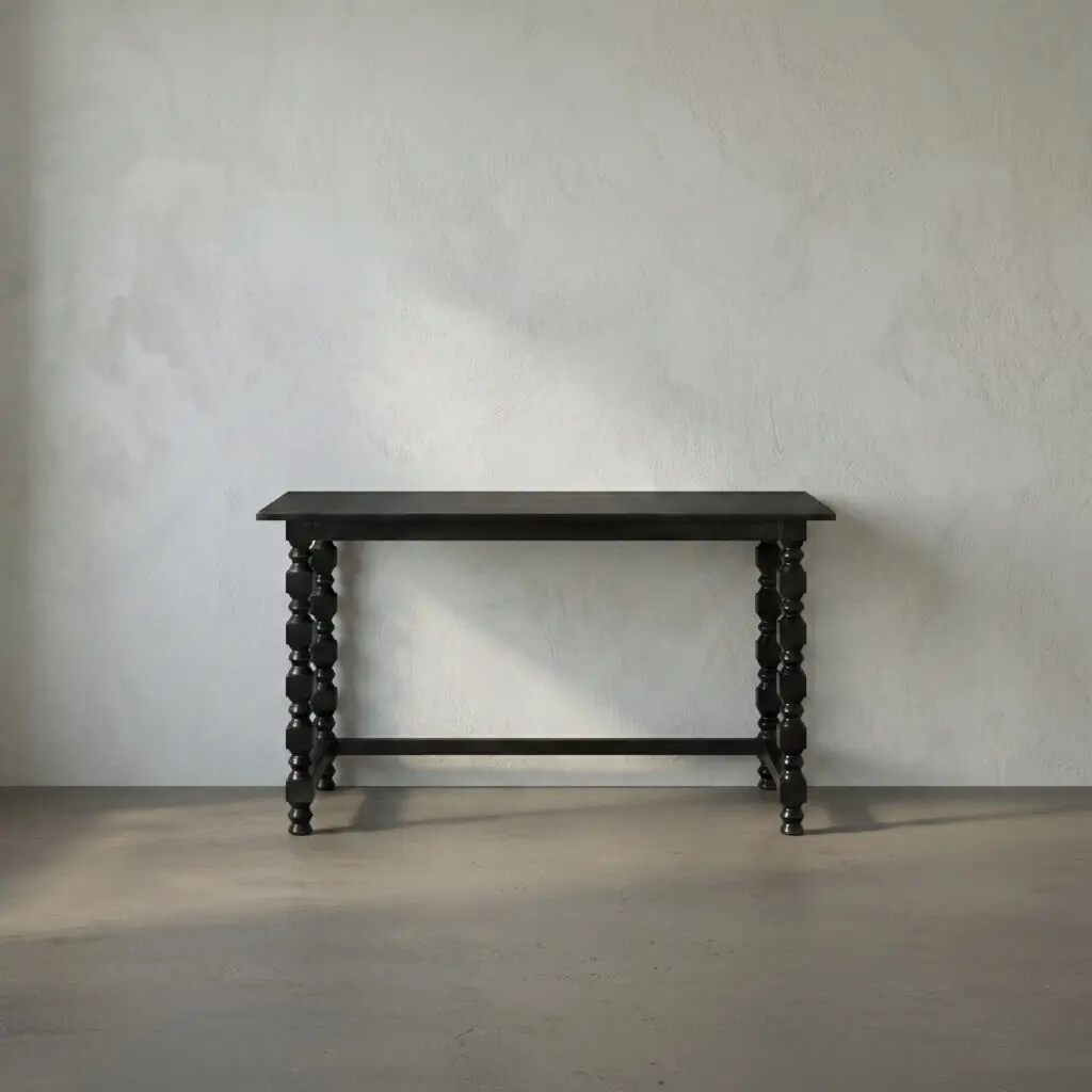 A dark wooden table with turned legs sits against a textured gray wall in a minimal room with a concrete floor.