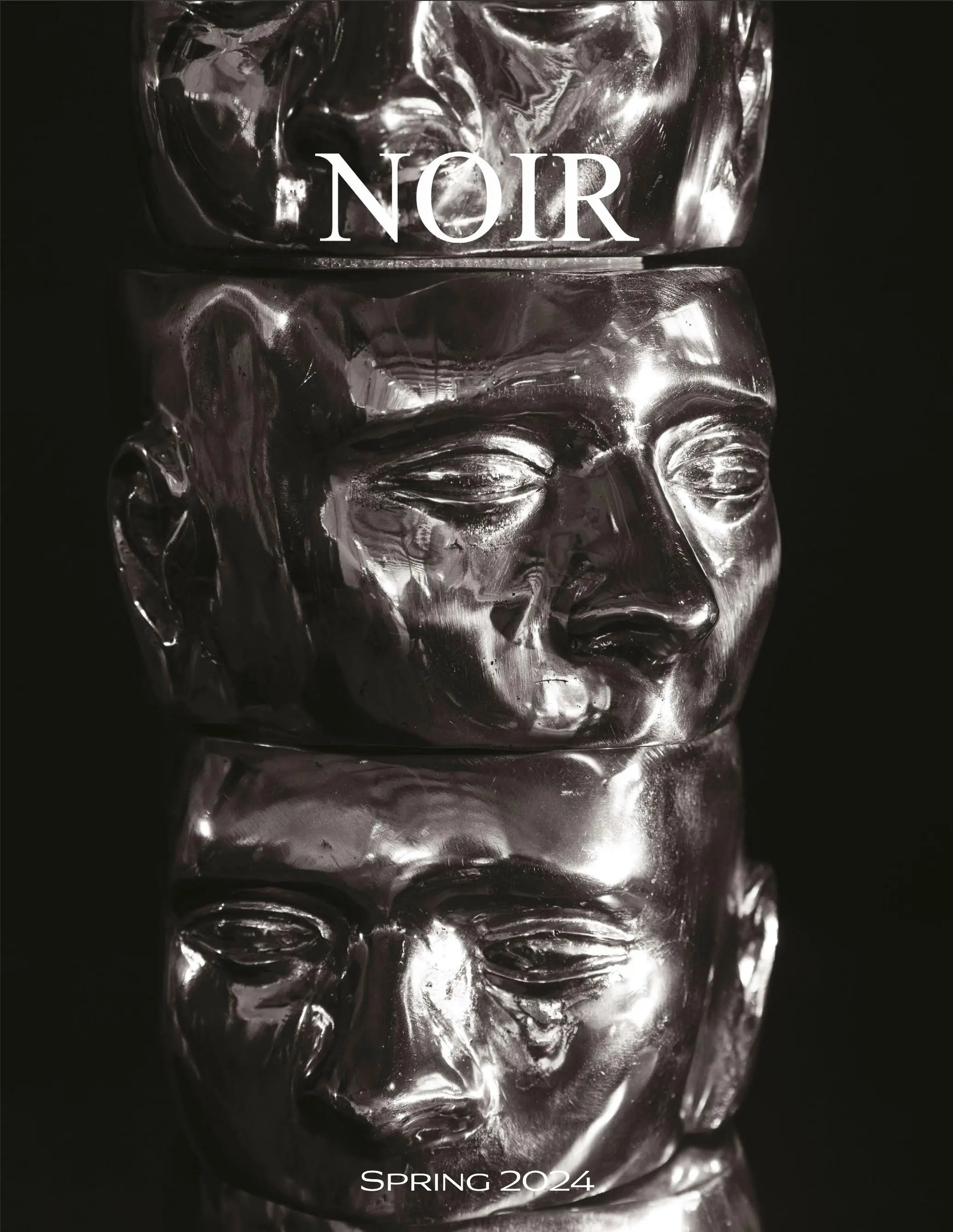 Close-up of a shiny metallic sculpture made of stacked carved faces, with the words SPRING 2024 at the bottom.