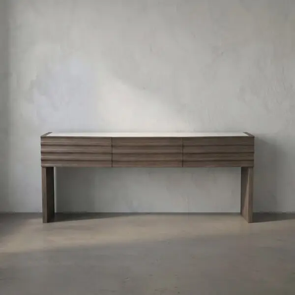 Minimalist wooden console table with three shallow drawers and square legs against a textured light wall.