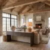 Cozy living room with exposed wooden beams, a stone fireplace, and large windows letting in natural light.