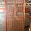 Antique wooden cabinet with carved panels and lattice doors, standing in a warehouse.