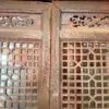Two weathered wooden lattice doors with central seam and decorative carved panels above the latticework.