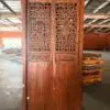 Large carved wooden cabinet with intricate lattice panels and floral motifs, standing in a warehouse floor with stacked pallets nearby.