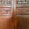 Wooden double doors with intricate carved floral panels at the bottom and geometric lattice above, separated by a central vertical seam and a thin wire across.