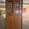 Large antique wooden cabinet with carved floral lattice doors in a warehouse setting.