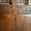Carved wooden doors with lattice panels and floral reliefs, separated by a vertical wooden beam.