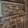 Dusty dark wooden panel with an ornate carved floral leaf motif on a weathered cabinet door.
