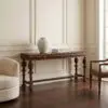 Cream paneled wall with a carved wooden console table, a large white ceramic vase, and two stacked design books on the table.