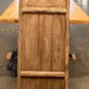 Wooden vintage pedestal with paneled doors and latticework on top, standing on a wooden platform in a workshop.