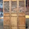 Three tall wooden folding screens with lattice panelwork placed in a warehouse, showing weathered panels and upper and lower solid frames